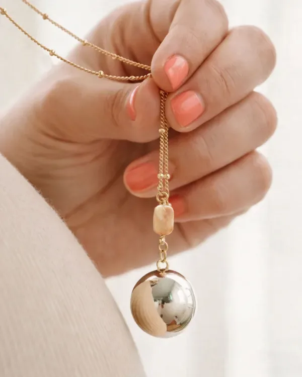 Hand holding a harmony ball pendant on a fine gold chain